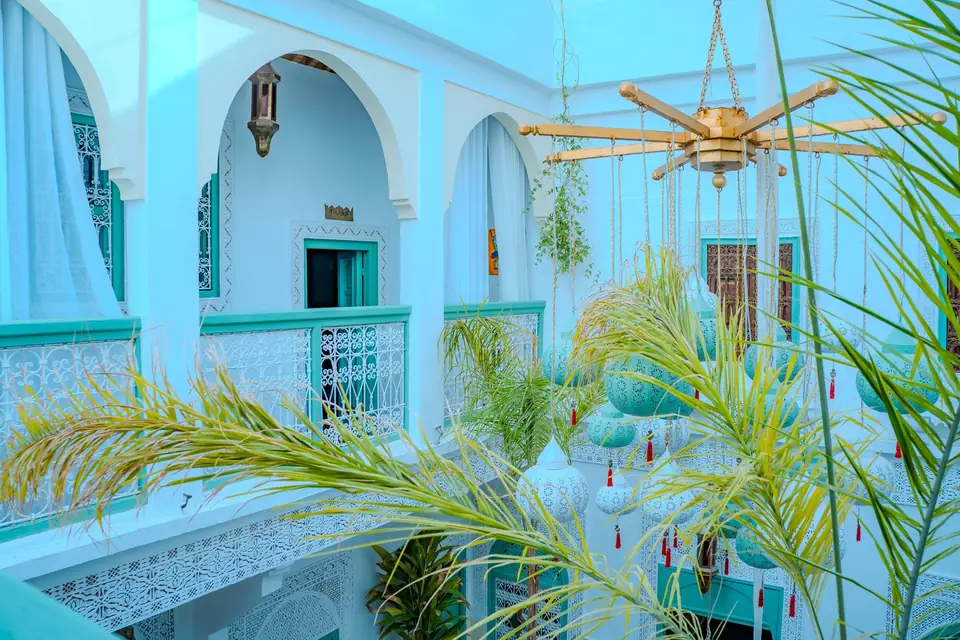 The riad's courtyard seen from the upper gallery, with carved white arches, palms and a brass lantern